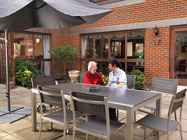 A nurse sitting and talking with a resident in the garden at Vicarage Farm Care Home