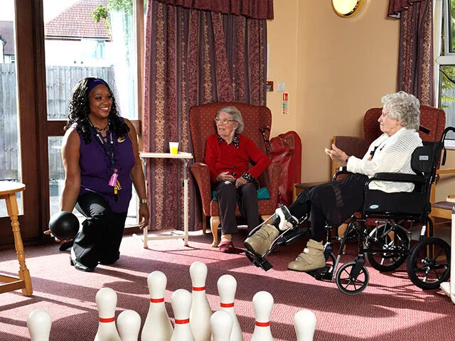 A care assistant leading a game with residents in the lounge at Vicarage Farm